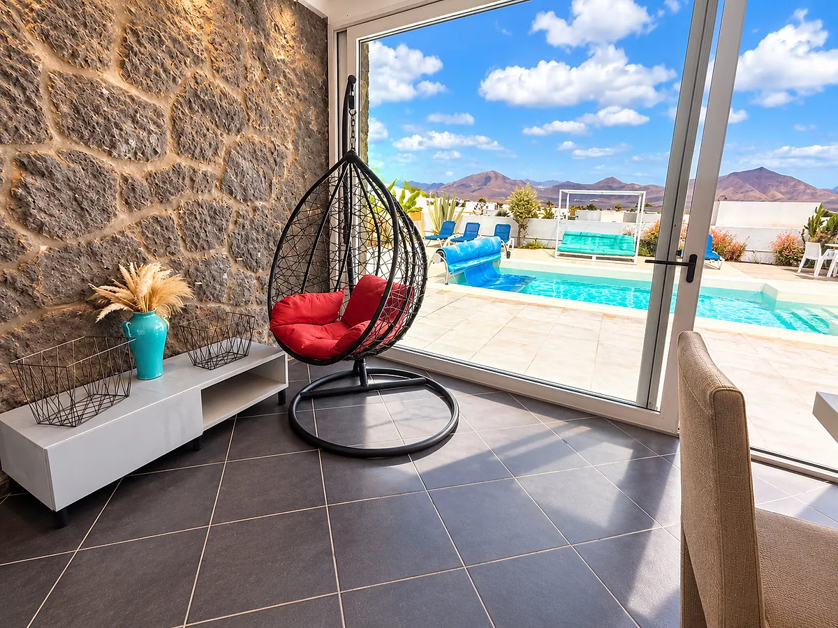 Sillón colgante junto a la pared de piedra y la puerta corredera hacia la piscina