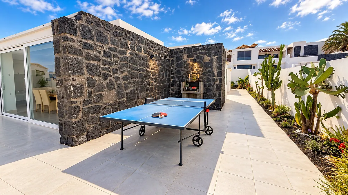 Patio lateral con mesa de ping pong y barbacoa junto a una pared de piedra volcánica