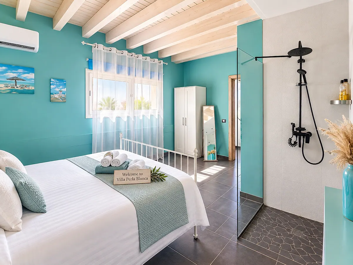 Dormitorio turquesa con cama doble, techo de vigas blancas y ducha de cristal